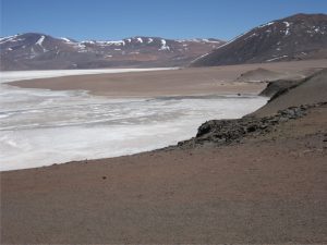 Alluvial fan lobes encroaching a gypsum-halite salar, Atacama, northern Chile. Right image shows an elevated fan (left centre) that represents deposition during a phase of higher lake levels; the older fan is now partly degraded. The cuspate and indented distal fan margin record a succession of fan lobes. Grey-brown colours reflect basalt-andesite clast compositions, enhanced by desert varnish.