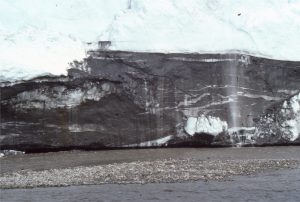 The edge of Muller Ice Cap on central Axel Heiberg Island, eroded by the outwash stream. Deformation of ice is accentuated by dark mud and sand in the ice (clear ice lies above the darker foundation. Ice rheology here includes ductile and brittle deformation. The lower sediment-rich section is about 4.5 m thick