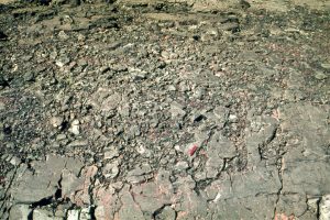 Cross-section through a lava flow-top breccia; the upper part is completely broken up by movement as the lava solidified. More coherent, less fragmented rock occurs below this (lower right), was deeper in the flow and cooled more slowly.