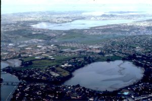 Panmure Basin, also tidal, is older than 17,000 years. The crater entrance is a narrow rocky channel, connected to Tamaki estuary - this is the Pacific Ocean side of Auckland. The stretch of water in the distance is part of Manukau Harbour - the Tasman Sea side of Auckland. A narrow isthmus separates the two ocean water bodies.  All three craters are rimmed by tephras. Lake and tidal basin sediment fill can also be used to date the events, using pollen and ash layers derived from more distant eruptions in Rotorua-Taupo.