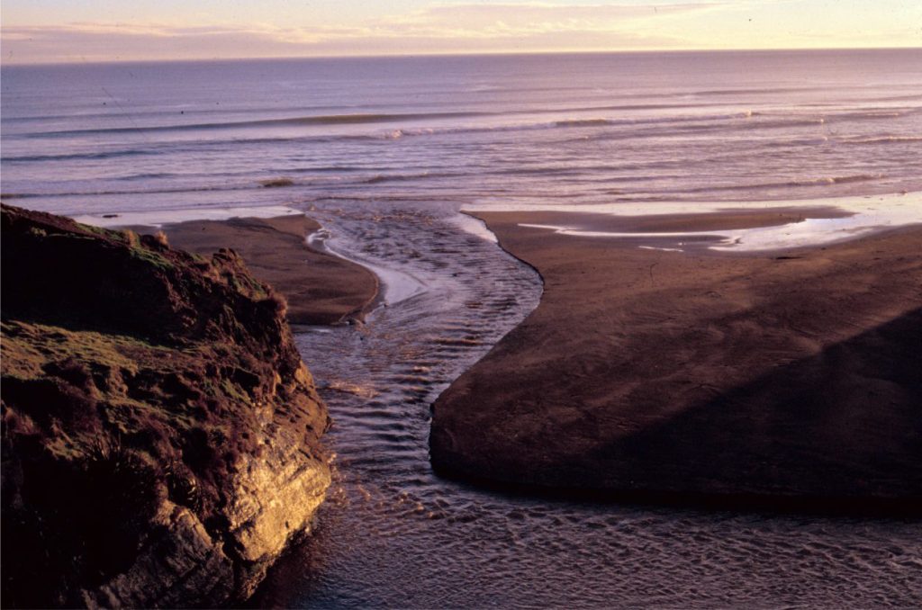 The meeting of waves – a train of supercritical stationary waves flowing towards the coast, subdued by incessant transverse gravity waves parallel to the coast. Manawapu, New Zealand.