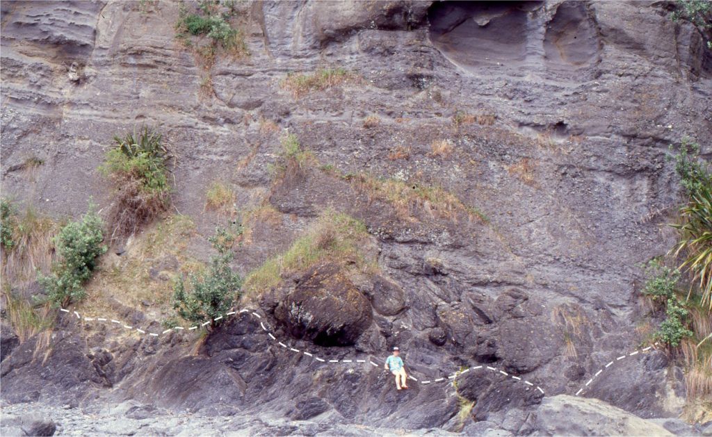 Lower Miocene shoreface-shelf pebble conglomerate and pebbly sandstone onlapping greywacke basement, Matheson’s Bay, north Auckland. The predominant lithofacies is low-angle crossbedding, with subordinate tabular crossbedding. The unconformity (dashed line) places Early Miocene shoreface deposits over Mesozoic – upper Paleozoic greywacke basement. Pockets of boulders overlie the unconformity.