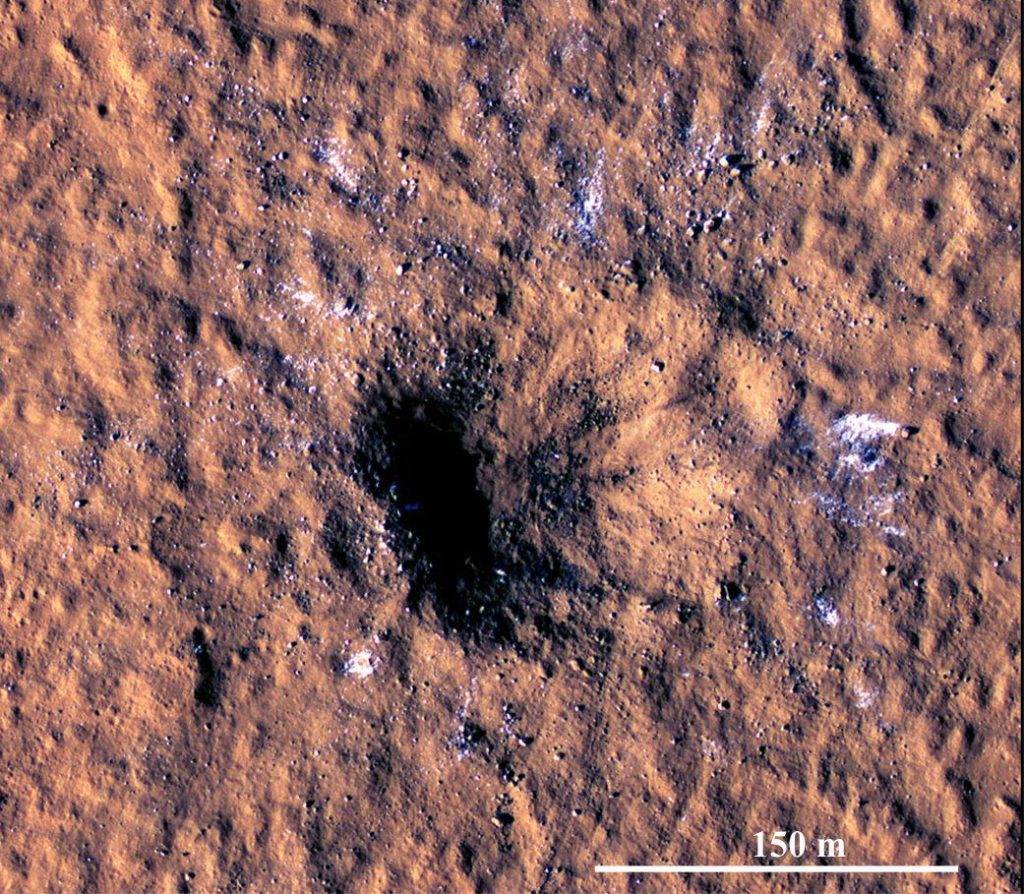 A HiRISE image of the S1094 crater in Amazonis Planitia taken 2-3 Sol after impact. The crater is asymmetric, about 150 m diameter and 21 m deep. Based on empirical models, the impactor was probably 5-12 m across (on Earth it would have burned up on entry). Posiolova et al., (op cit.) calculate the angle of impact at about 30o – the ejecta blanket extends up to 37 km from the crater because of this low angle. White debris in the ejecta is thought to be water ice. Image Credit: NASA/JPL-Caltech/University of Arizona. 