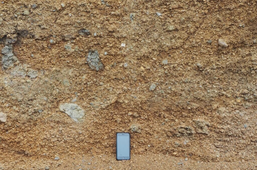 The well-bedded nature of the volcaniclastic deposits seen from a distance, is less obvious in closer views because clast sorting in each layer is poor, and the change in grain size between layers subtle. The largest clasts in this view are 15 cm maximum length – there is no preferred clast orientation. 